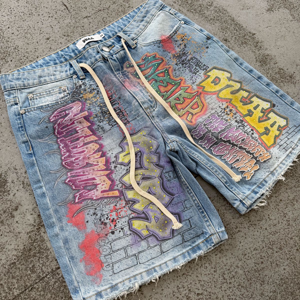 DUAA Shorts - shorts de denim lavado claro con estampado de graffiti, foto en plano